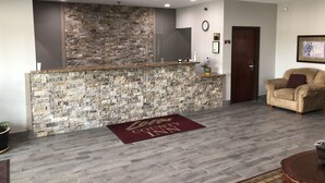 A reception area with a stone wall, a reception desk, a clock, and a door. - Lea County Inn (Hobbs)