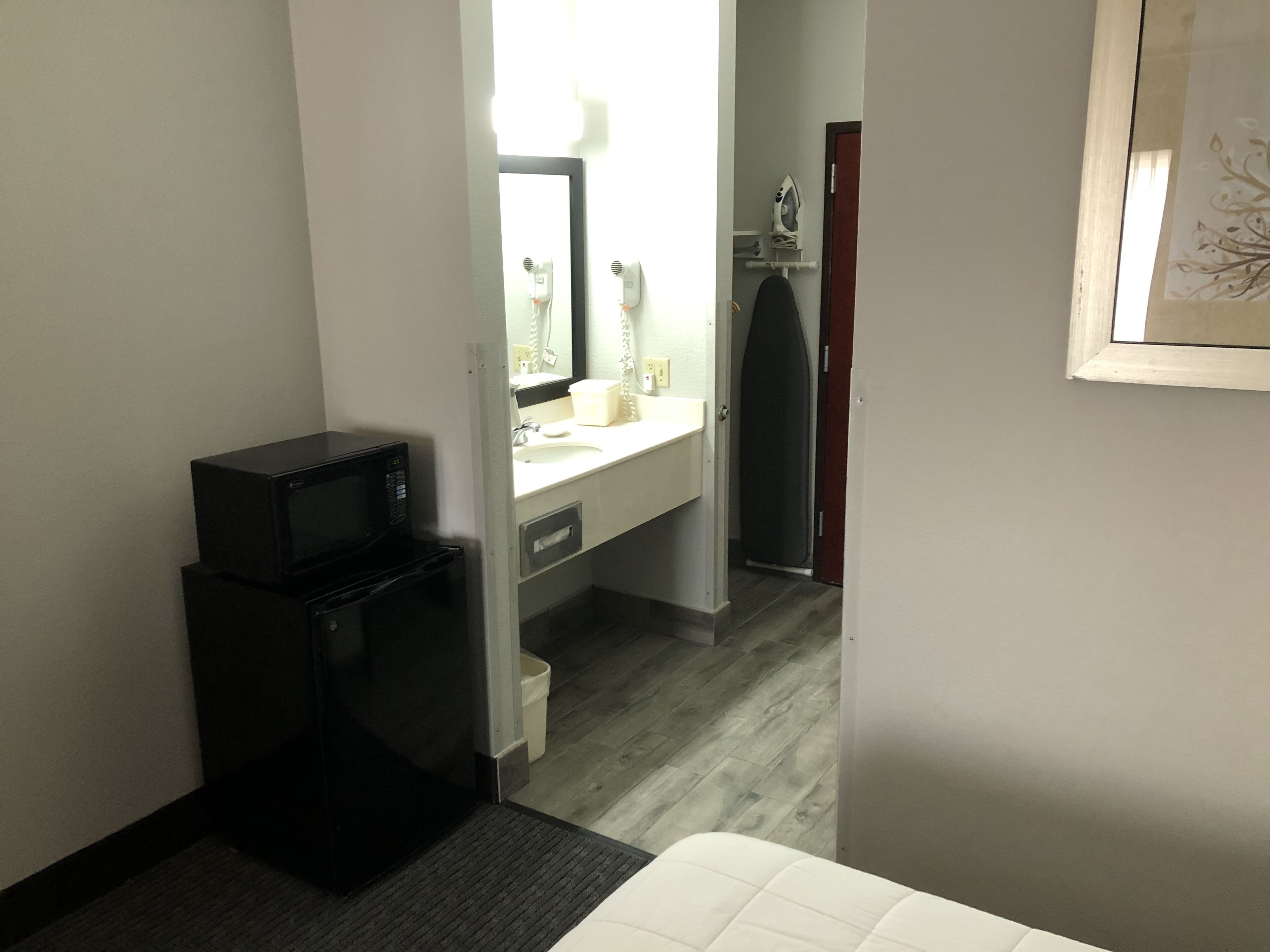 A hotel room with a compact kitchenette, a small refrigerator, a microwave, a sink, and a mirror.