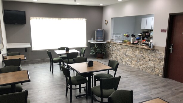A restaurant with wooden tables and chairs, a kitchen area, and a clock on the wall. - Lea County Inn (Hobbs)