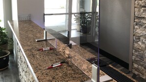 A reception area with a granite counter, a potted plant, a keyboard, and a glass partition. - Lea County Inn (Hobbs)