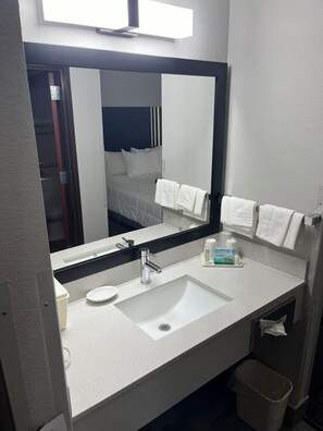 A hotel bathroom with a white sink, a mirror, a towel rack, and a trash bin.