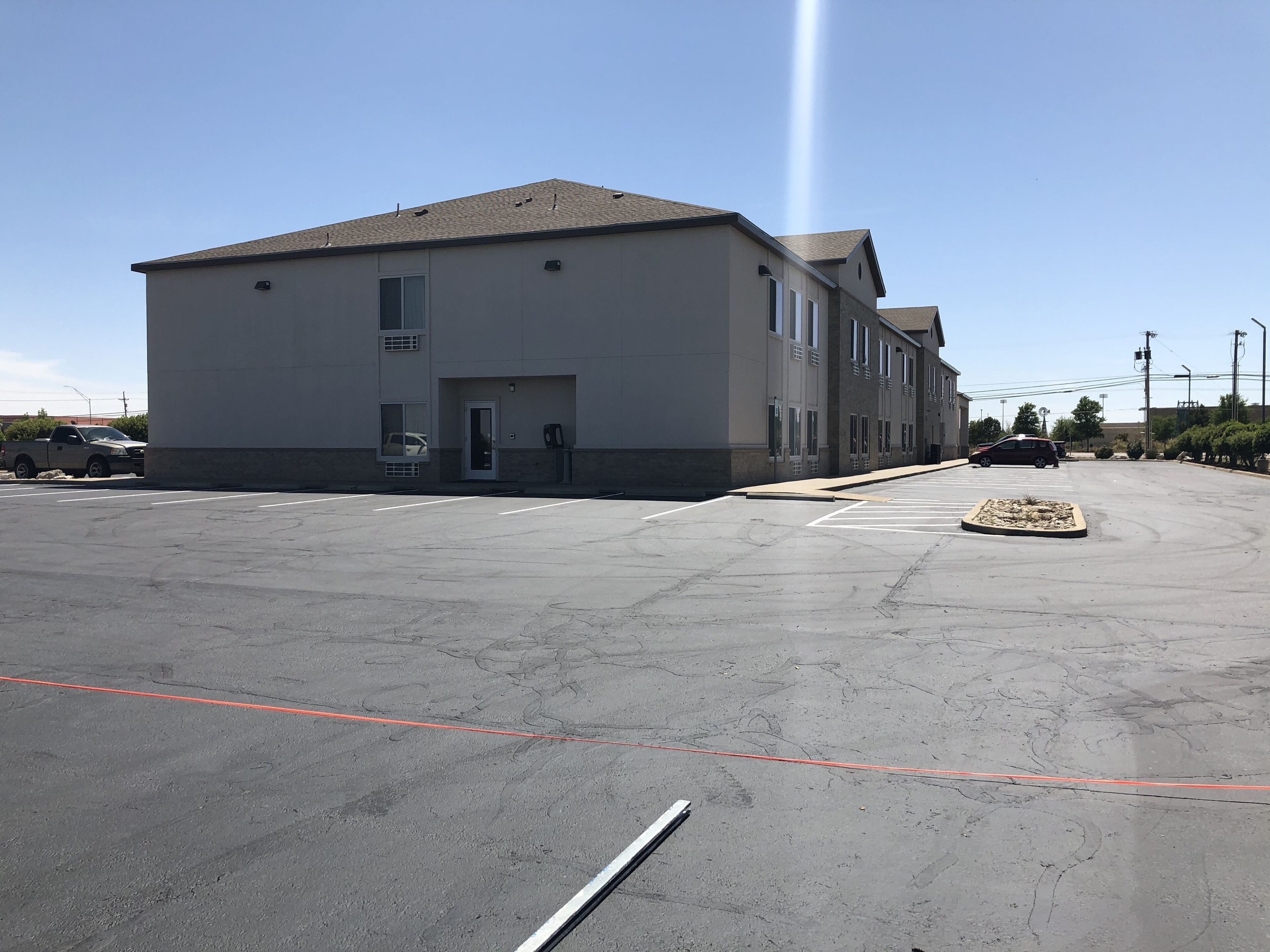 A large, single-story building with a flat roof and a grey facade. There are multiple windows on the front and side of the building. The parking lot in front of the building is empty, with a few cars parked in the distance.