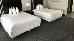 A hotel room with two beds, a nightstand, a lamp, and a framed picture on the wall. - Lea County Inn (Hobbs)