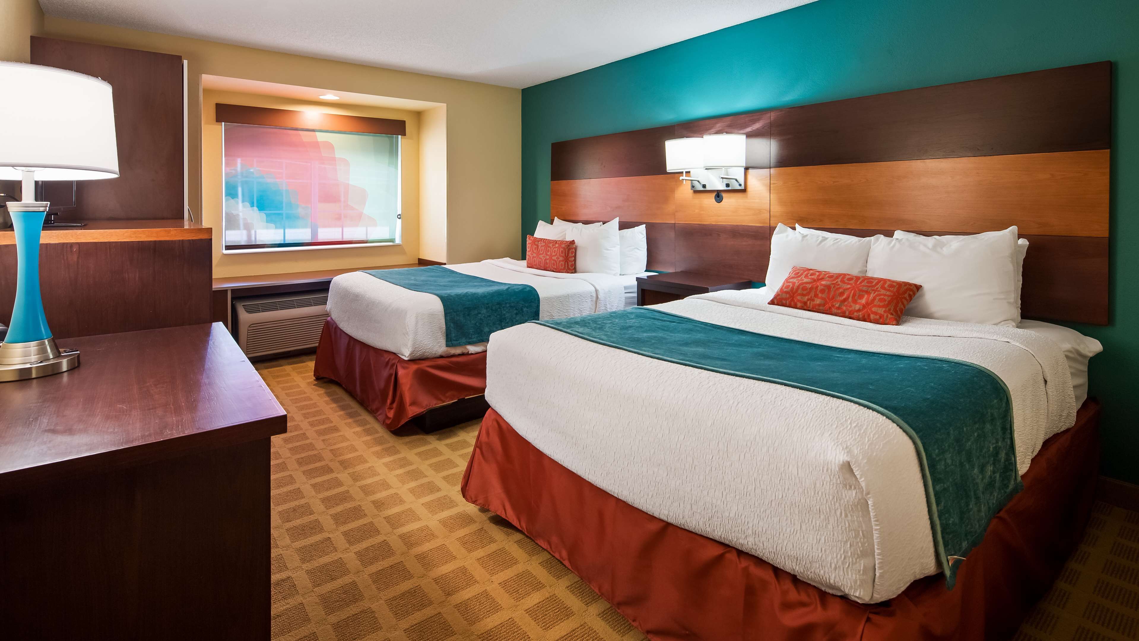 A hotel room with two beds, a desk, a lamp, and a window with a view.