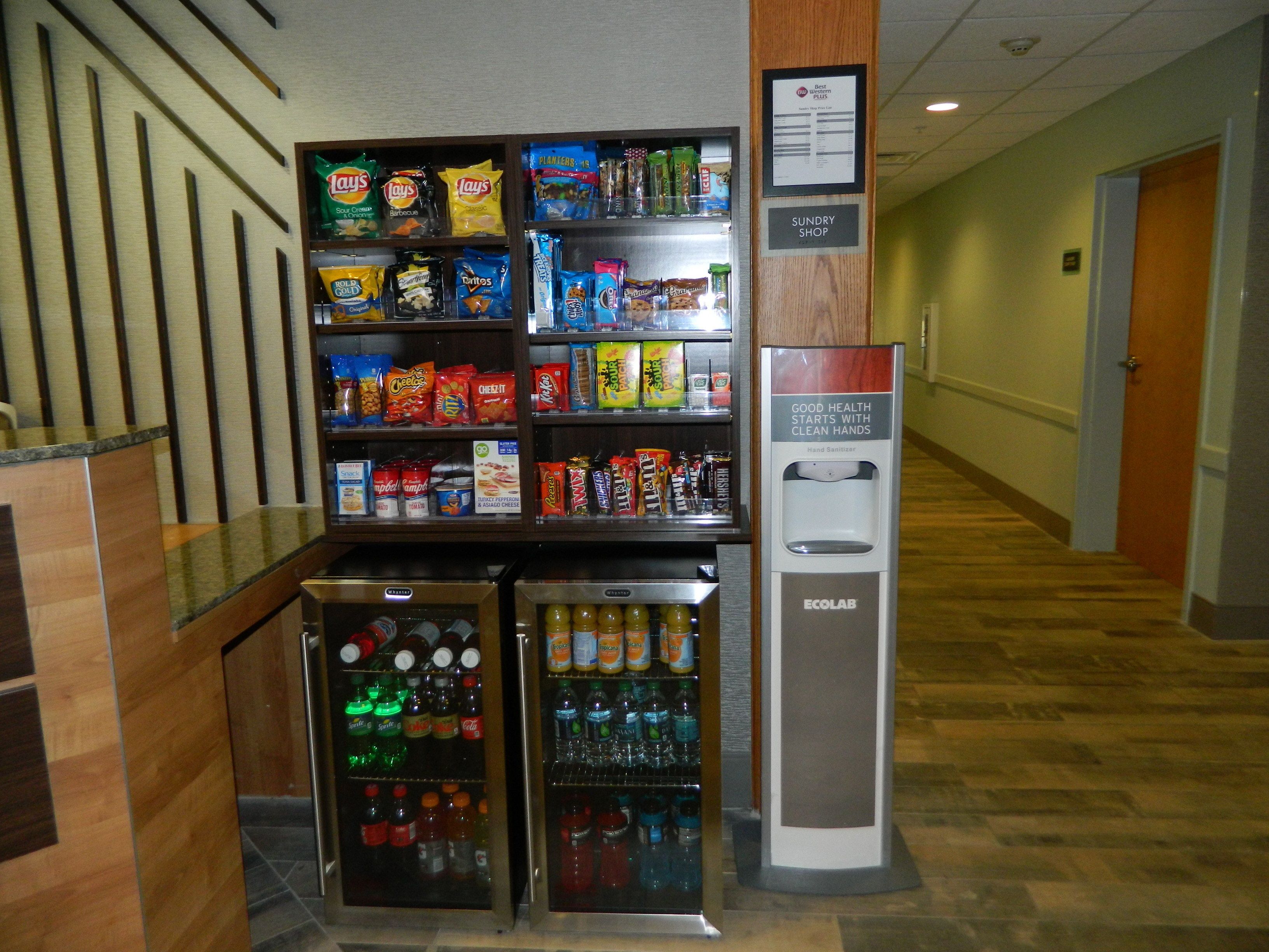 A vending machine with snacks and drinks, a hand sanitizer dispenser, and a sign for the sundry shop.