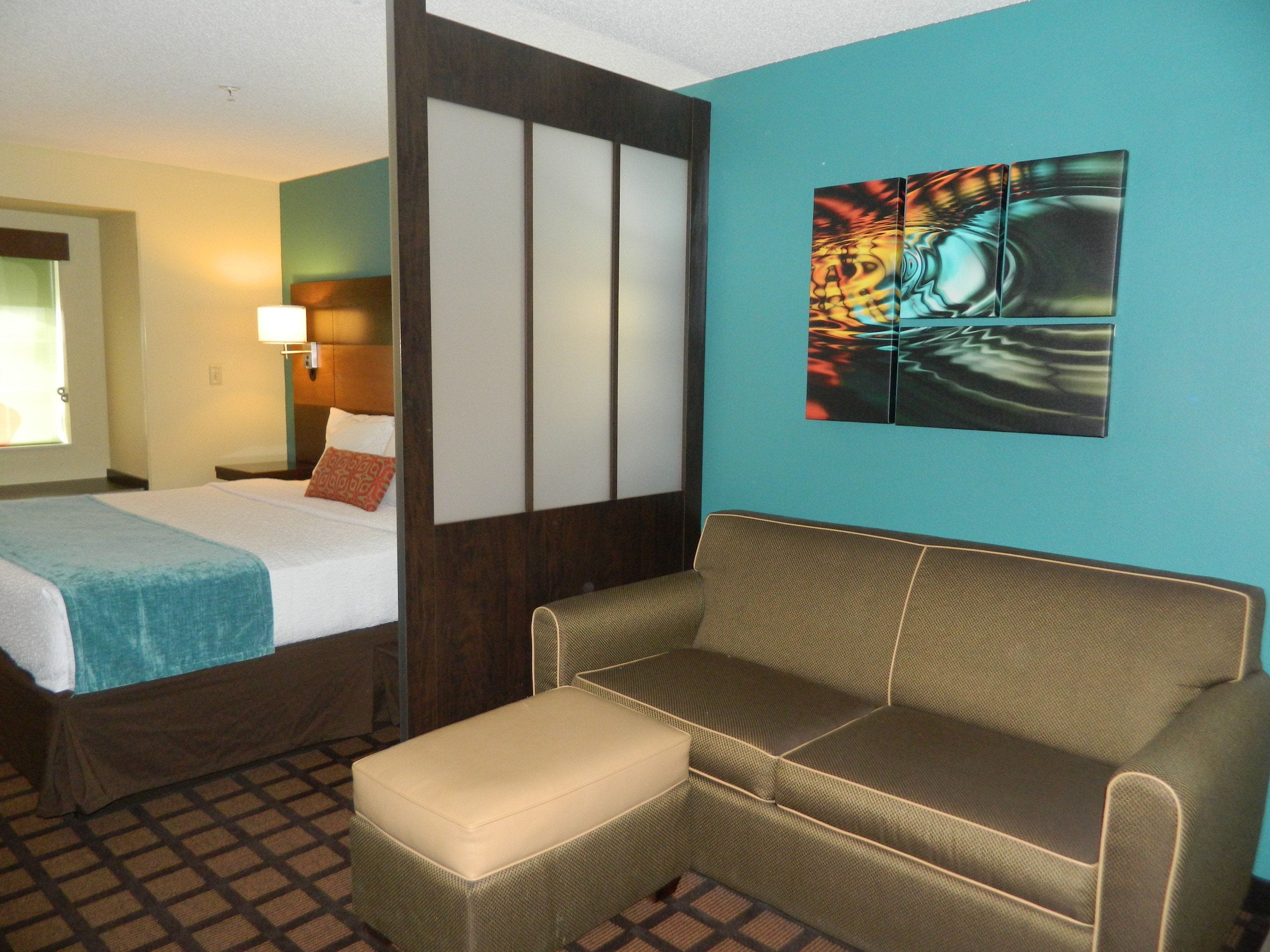 A hotel room with a bed, a sofa, a small table, and a painting on the wall.