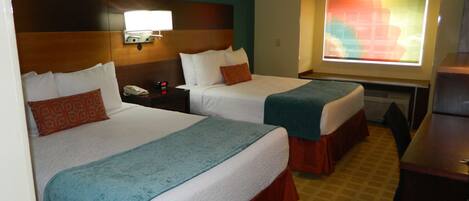 A hotel room with two beds, a desk, and a television.
