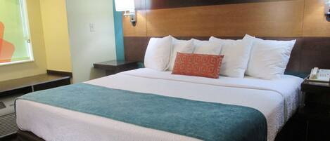 A hotel room with a large bed, a nightstand with a phone, and a wall-mounted lamp.