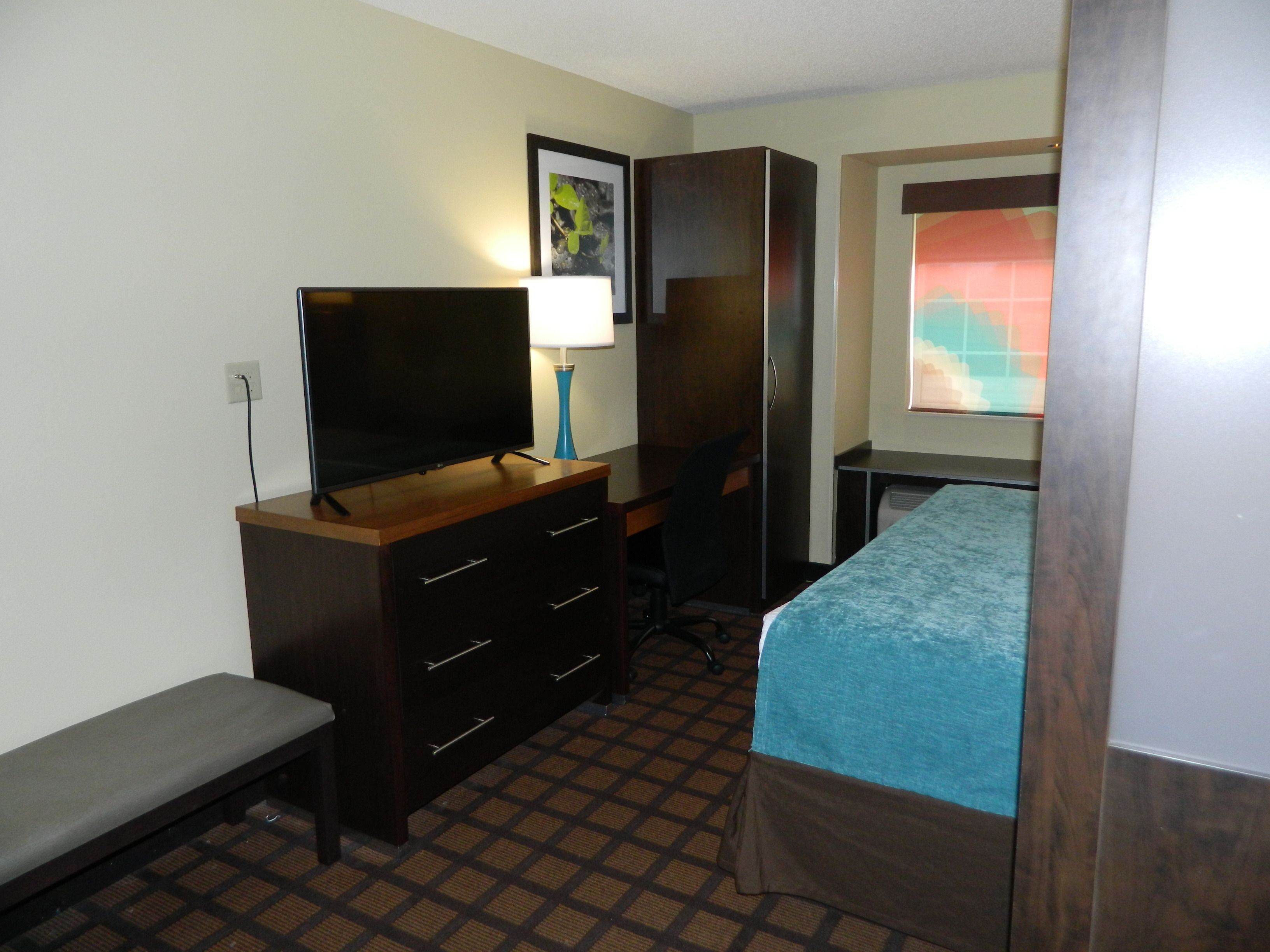 Een hotelkamer met een bed, een bureau met een televisie, een lamp en een garderobe.