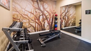 Un gimnasio con equipo de ejercicio, un espejo y una pared con un mural de un árbol.