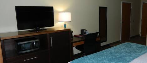 Una habitación de hotel con cama, escritorio con computadora, televisor, microondas y lámpara.