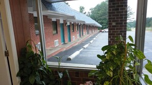 Blick durch ein Fenster auf eine Reihe von Ziegelgebäuden mit einem Parkplatz davor.