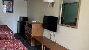 Ein Hotelzimmer mit zwei Betten, einem Schreibtisch, einem Fernseher, einem Spiegel und einer Lampe.