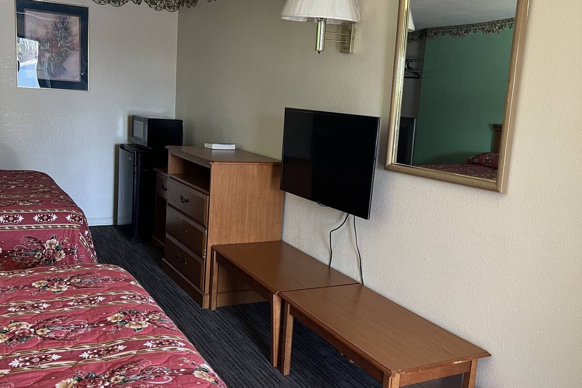Une chambre d’hôtel avec deux lits, un bureau, une télévision, un miroir et une lampe.
