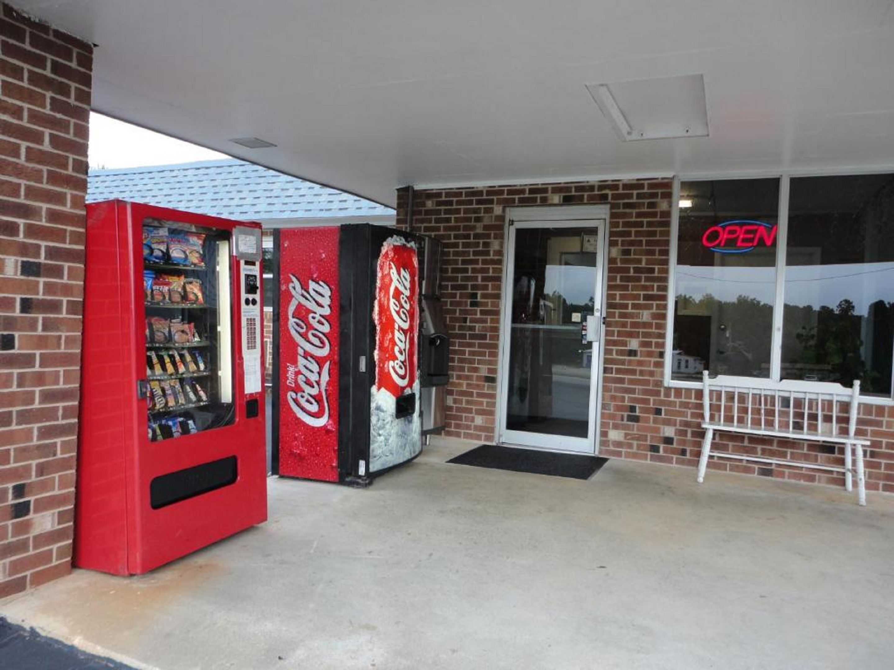 Una macchina automatica di Coca-Cola davanti a un edificio con facciata in mattoni e porta in vetro.