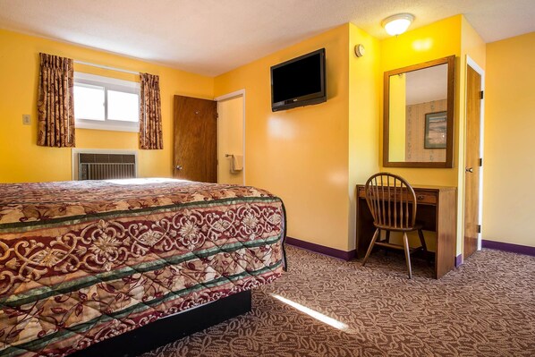 Une chambre d’hôtel avec un lit, un bureau, une chaise, une télévision et un miroir.