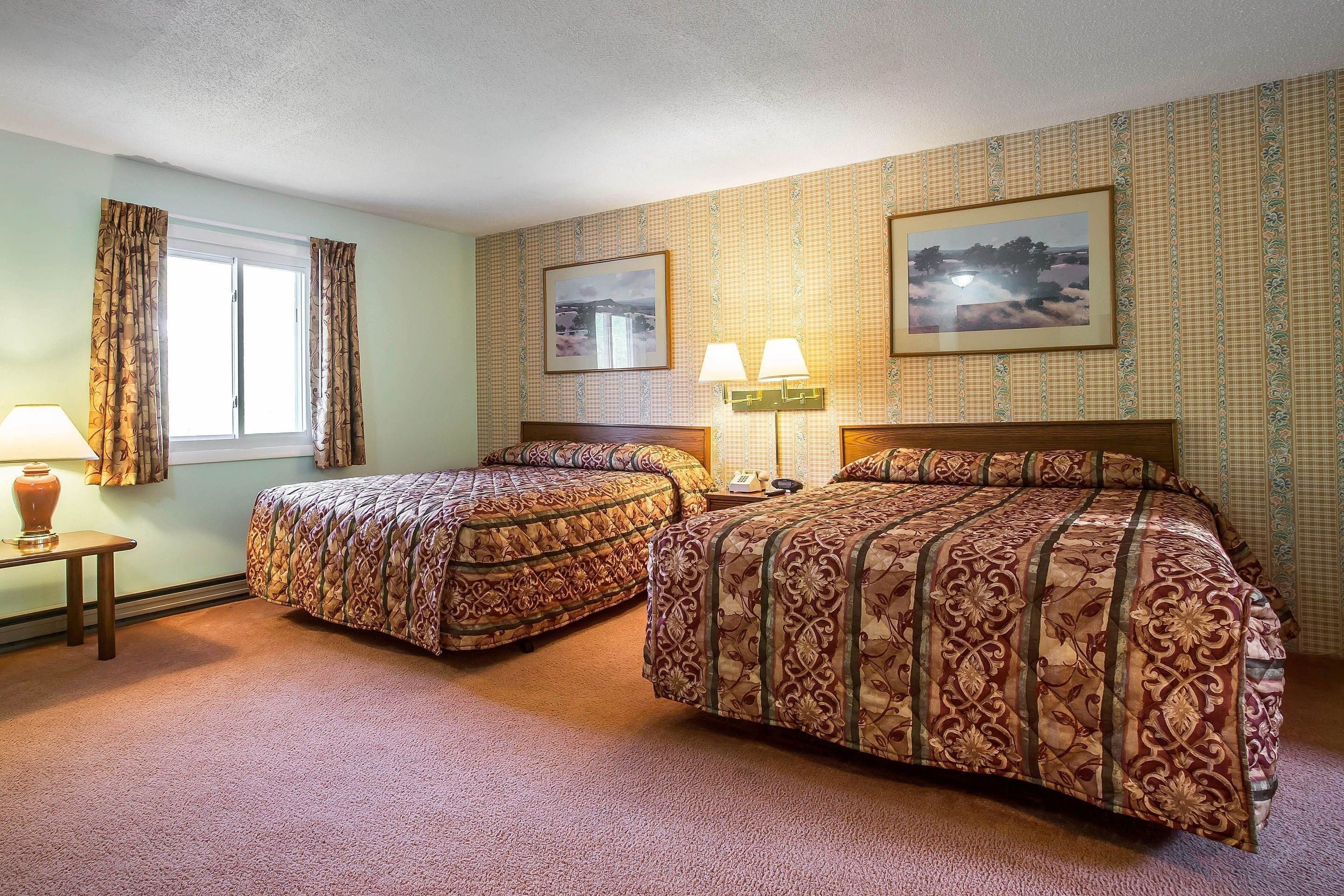 Quarto de hotel com duas camas, uma mesa de cabeceira, um abajur e duas luminárias na parede.
