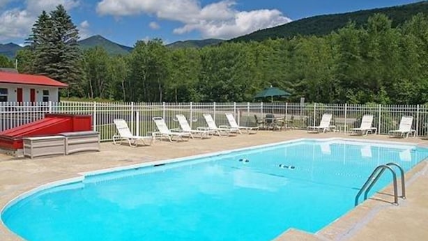 A swimming pool with lounge chairs and a red building in the background. - Rodeway Inn Lincoln I-93 (Lincoln)