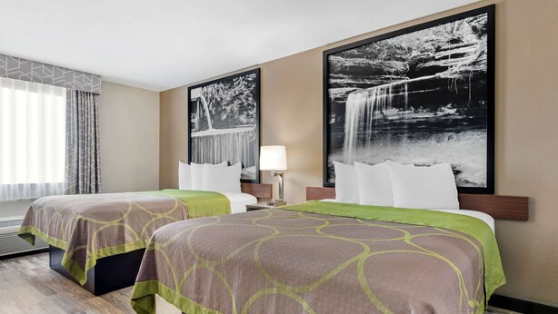 Ein Hotelzimmer mit zwei Betten, einem großen Fenster mit durchsichtigen Vorhängen, einer Wandlampe und zwei großen Schwarz-Weiß-Fotografien von Wasserfällen.