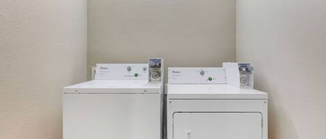 Deux lave-linge à chargement frontal Whirlpool blancs, dans une buanderie, avec un luminaire au-dessus.