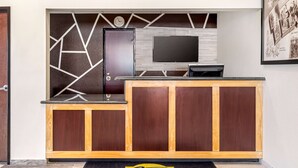 Ein Empfangsbereich mit Holztresen, einem an einer Wand mit geometrischem Muster befestigten Flachbildfernseher und einem gerahmten Willkommensschild.