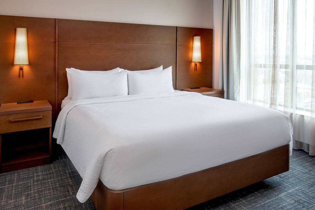 A hotel room with a large bed, wooden headboard, two bedside tables, and wall-mounted lamps.