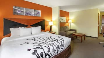 Un cuarto de hotel con una cama grande, dos lámparas de noche, una mesita, un sofá y obras de arte en las paredes.