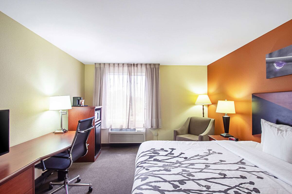 A hotel room with a bed, desk, chair, and a window with curtains.