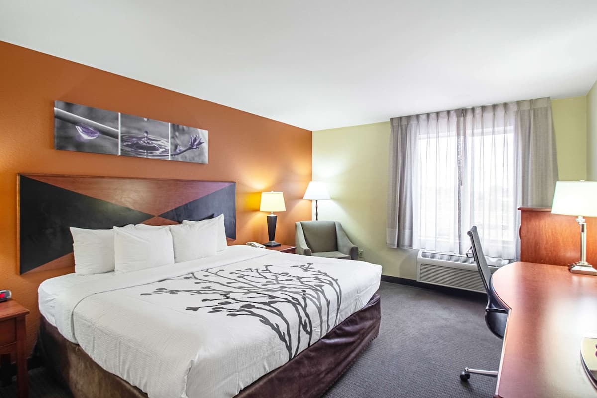 A hotel room with a large bed, a desk, a chair, a lamp, and a window with curtains.