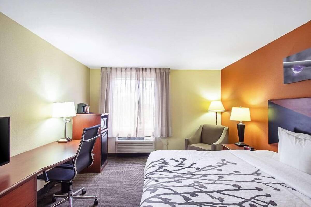 A hotel room with a bed, desk, chair, and two lamps.