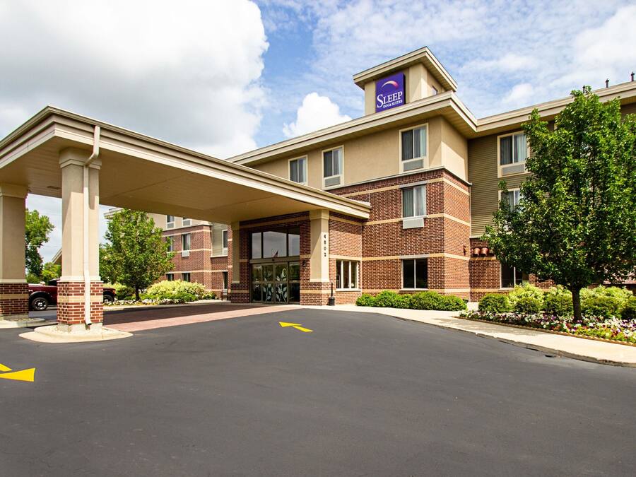 Een hotel met een overdekte ingang, gevel van baksteen en een bord waarop staat Sleep Inn & Suites.