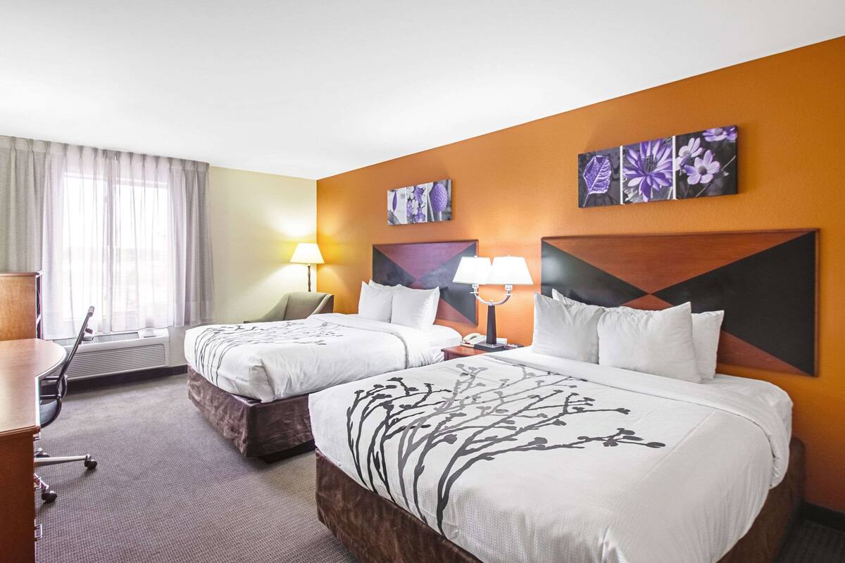 A hotel room with two beds, a desk, a chair, and a window with curtains.