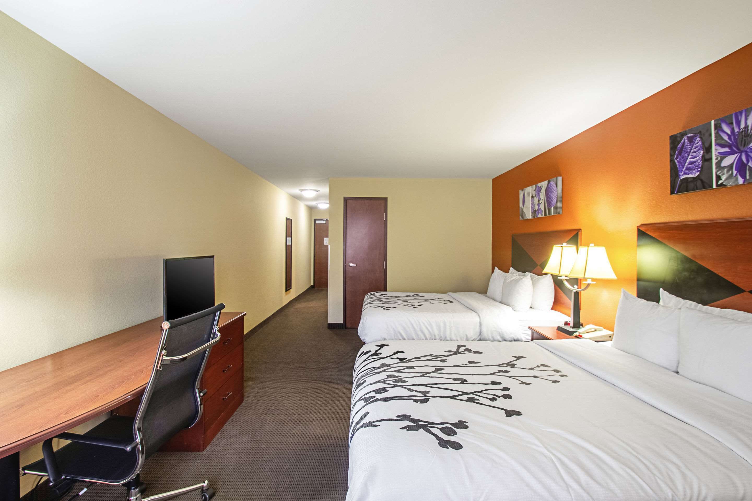 A hotel room with a desk, two beds, a TV, and a painting on the wall.