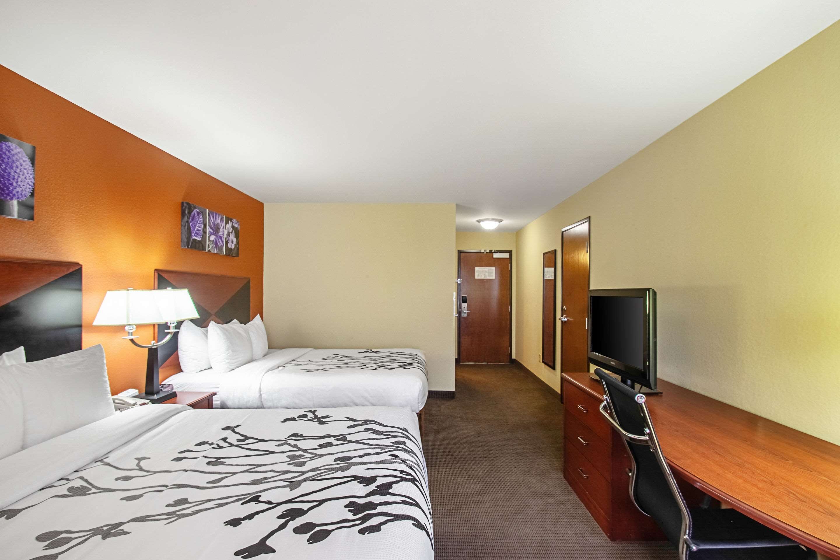 Ein Hotelzimmer mit zwei Betten, einem Schreibtisch mit Fernseher und einer Lampe.