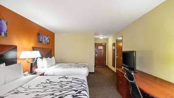 Ein Hotelzimmer mit zwei Betten, einem Schreibtisch mit Fernseher und einer Lampe.