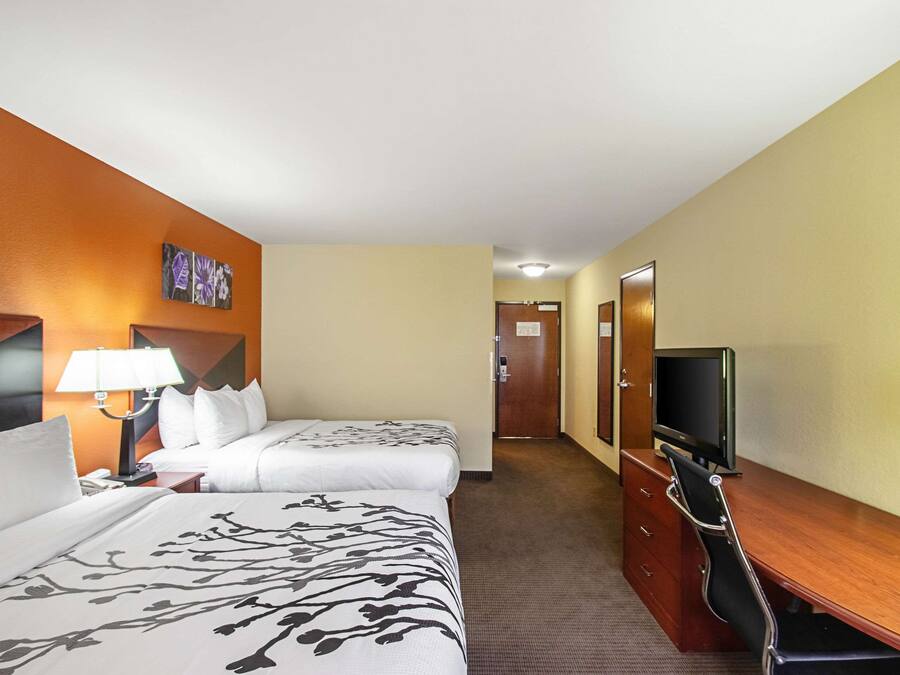 Ein Hotelzimmer mit zwei Betten, einem Schreibtisch mit Fernseher und einer Lampe.