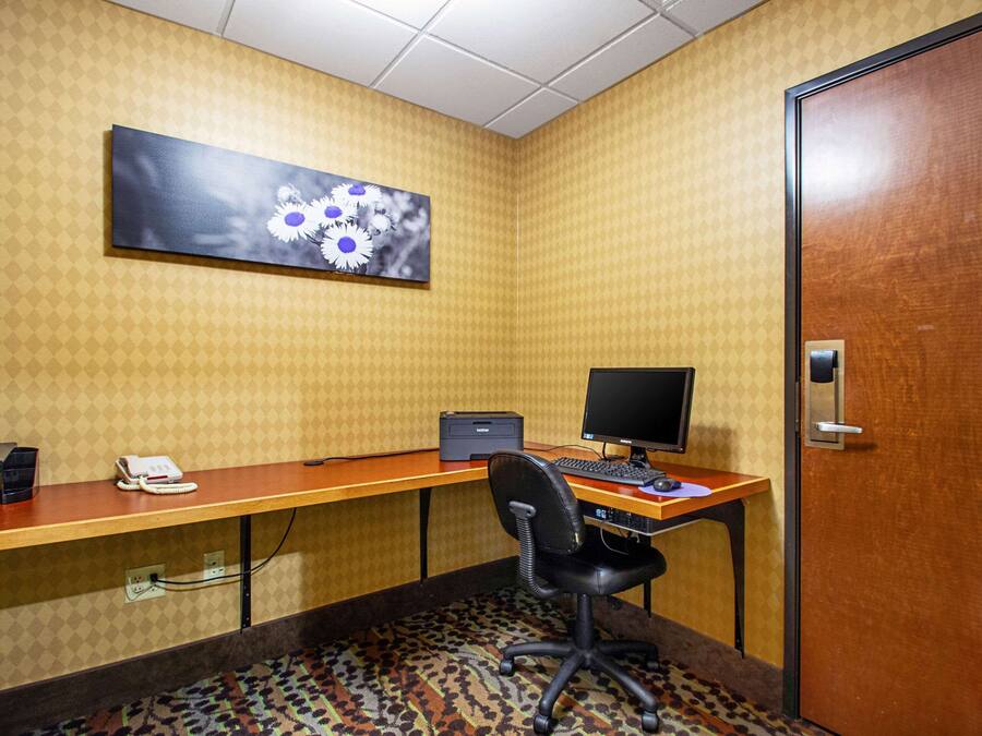 Ein Hotelzimmer mit einem Holztisch, einem Computer, einem Telefon und einem Gemälde an der Wand.