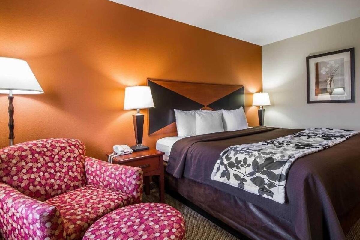 A hotel room with a bed, two bedside lamps, a chair, and a framed picture on the wall.