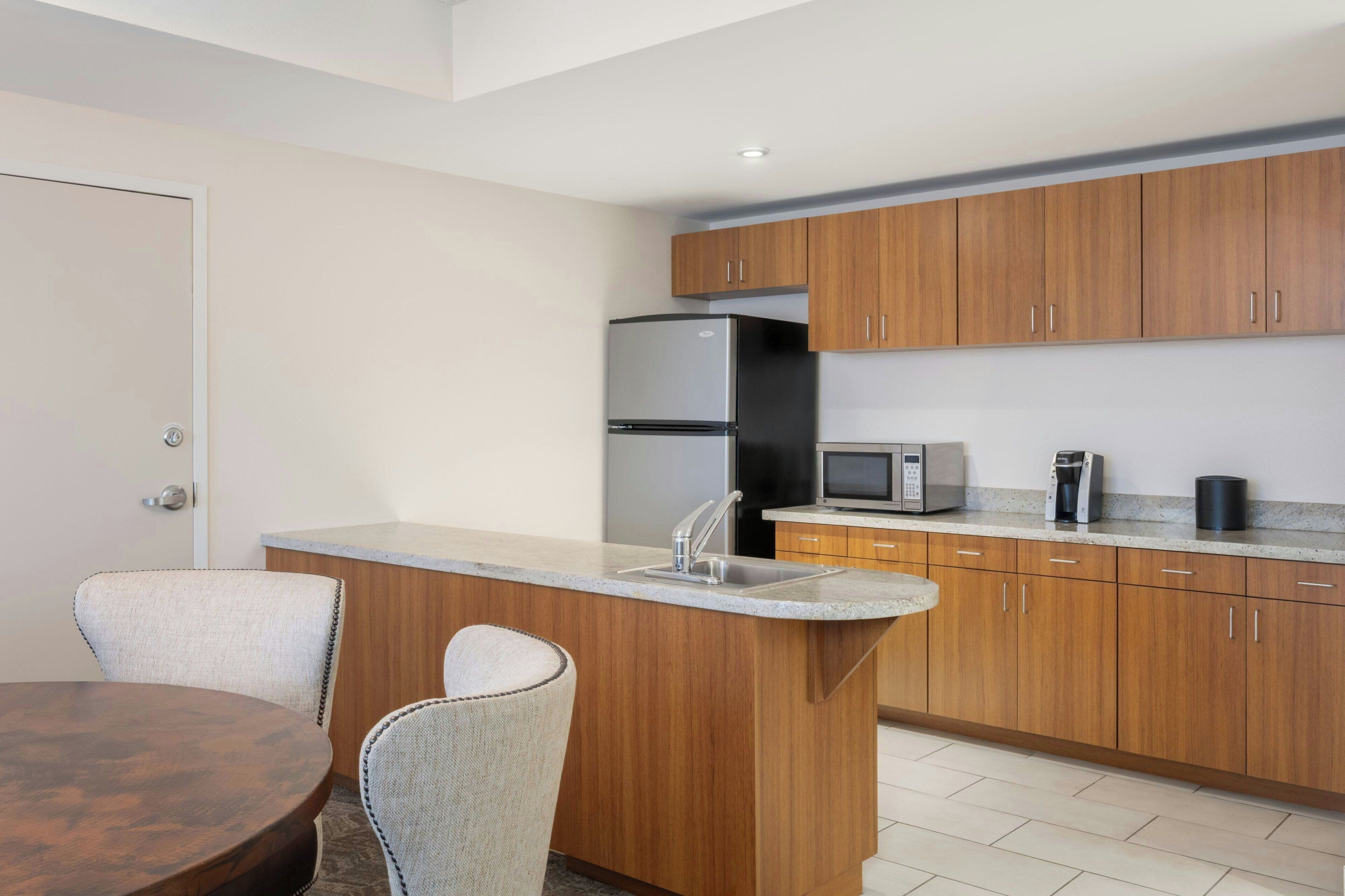 A modern kitchen with wooden cabinets, a stainless steel refrigerator, a microwave, and a coffee maker.