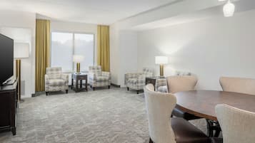 Habitación de hotel con una cama grande, televisión, escritorio con silla y mesa de comedor con sillas.