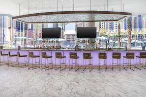 A bar area with a curved counter, multiple bar stools, and a view of tall buildings through large windows.