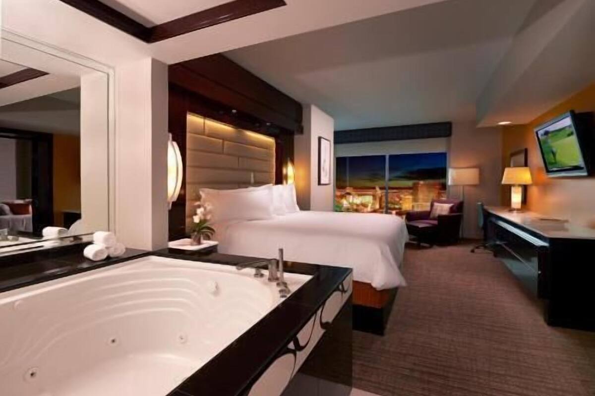 Een hotelkamer met een groot bad, een bed, een bureau en een televisie.