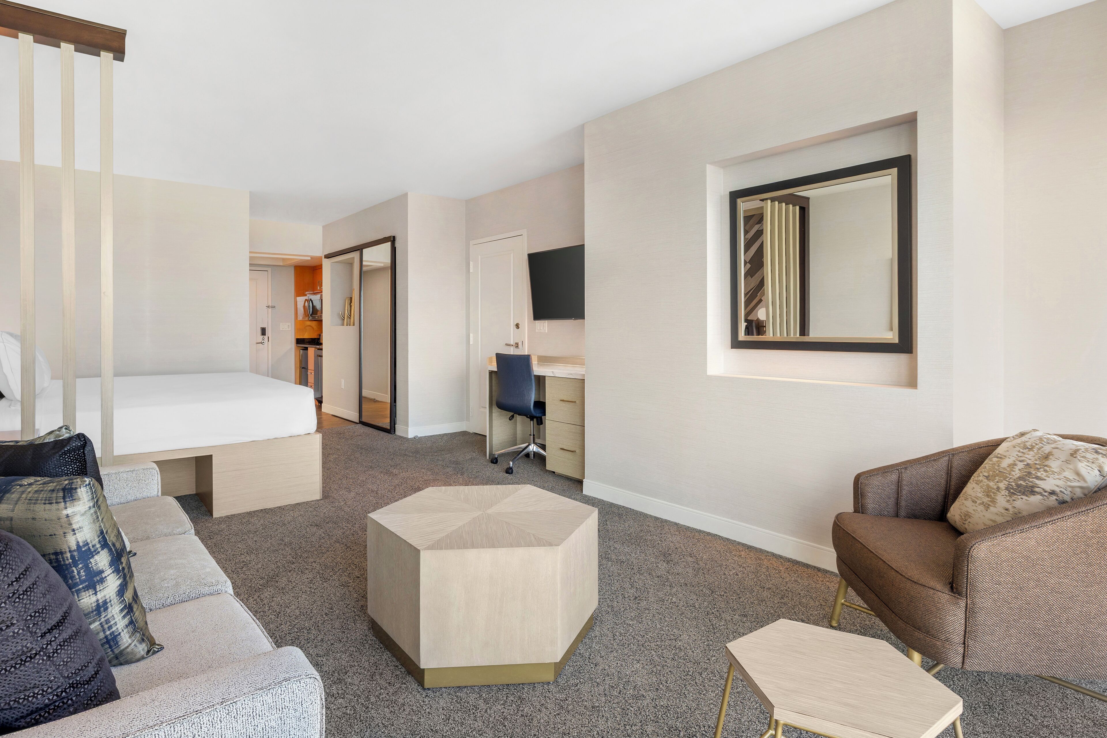 A modern hotel room with a sofa, a small coffee table, a desk, and a large mirror.