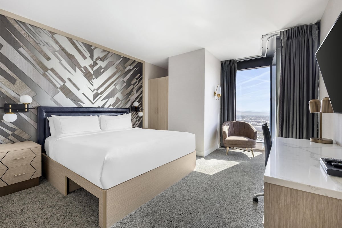 Een moderne hotelkamer met een groot bed, een bureau, een stoel en uitzicht op de stad.
