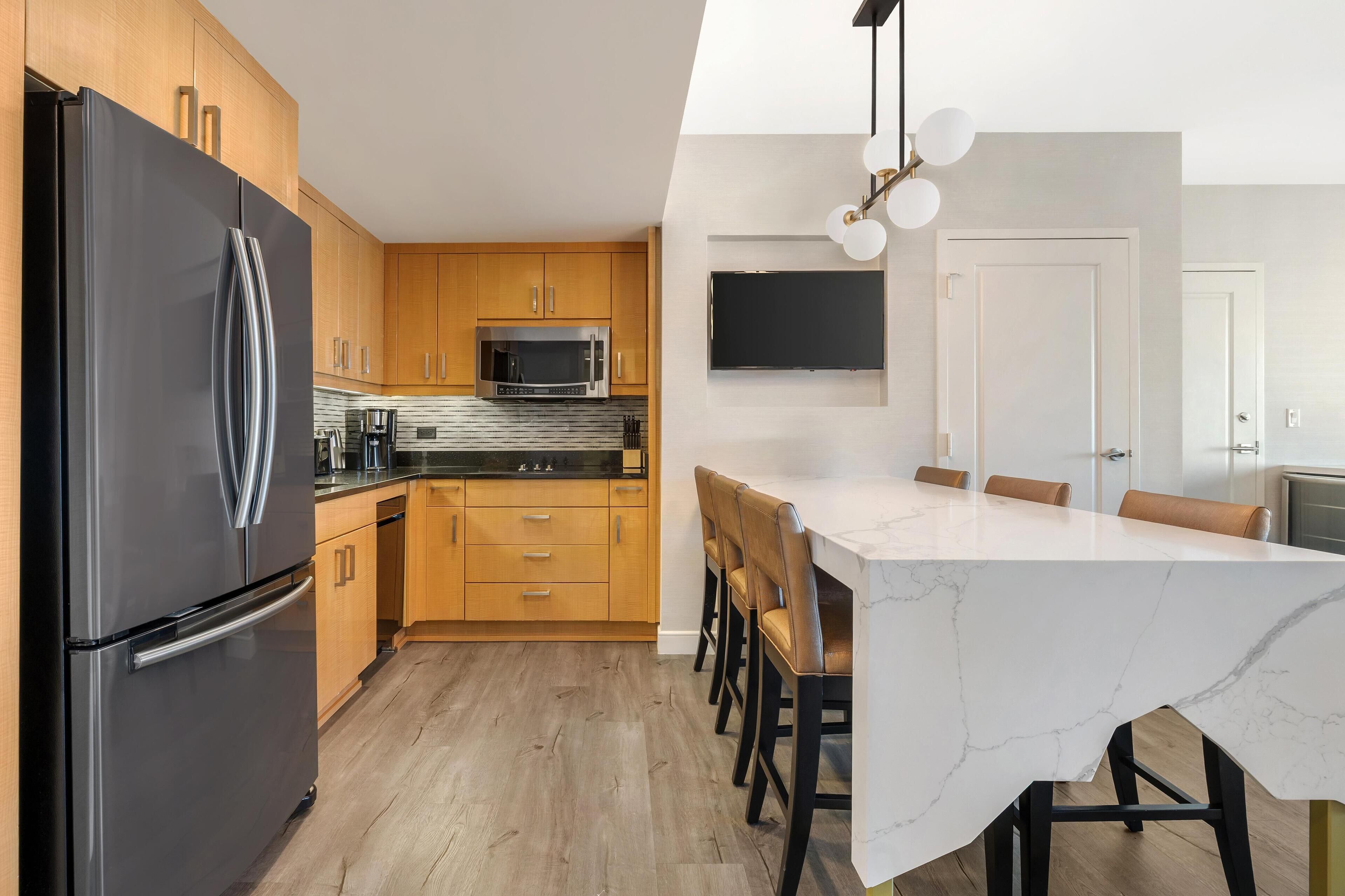 A modern kitchen with wooden cabinets, a black refrigerator, a microwave, and a large island with chairs.