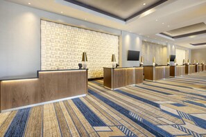 A hotel reception area with a patterned wall, multiple reception desks, and a patterned carpet.