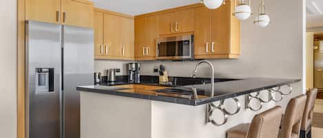 A modern kitchen with stainless steel appliances, wooden cabinets, and a central island with bar stools.