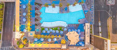 An aerial view of a hotel with a large pool, multiple lounge areas, and a parking lot.