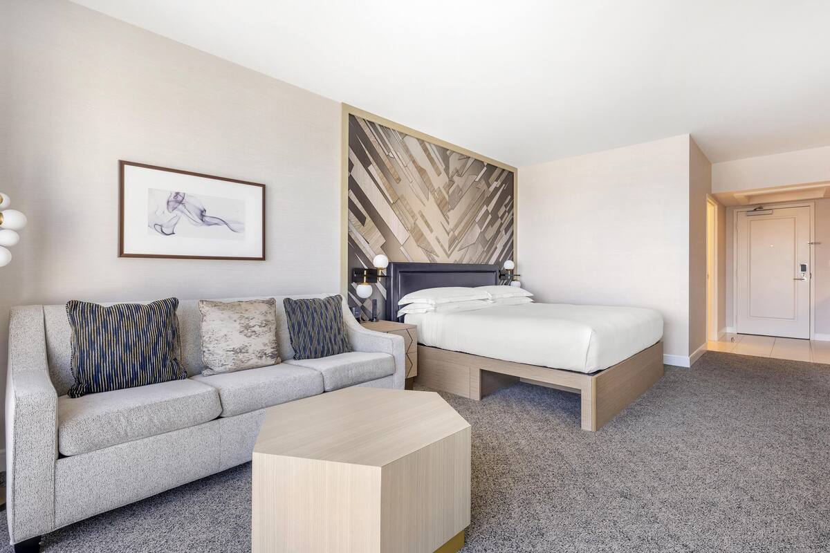 Een moderne hotelkamer met een bed, een bank, een bijzettafeltje en een wand met een geometrisch patroon.