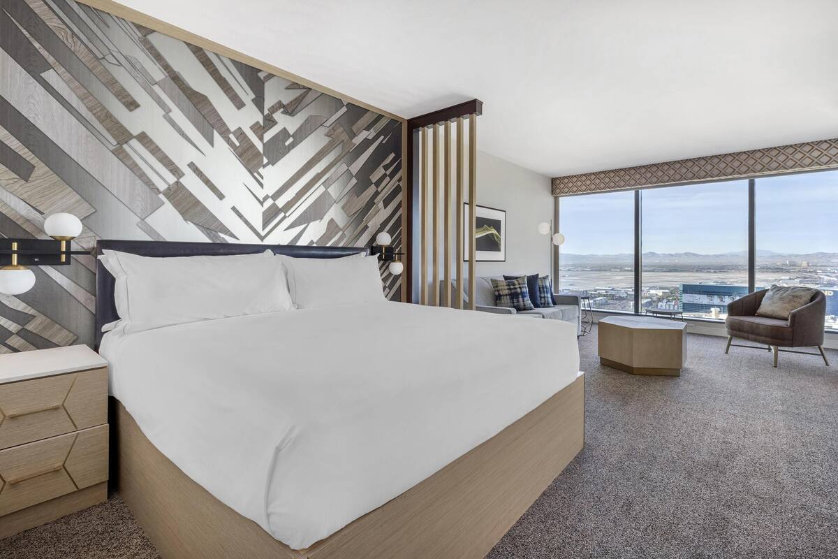 Een moderne hotelkamer met een groot bed, een bureau, een stoel en uitzicht op de stad.
